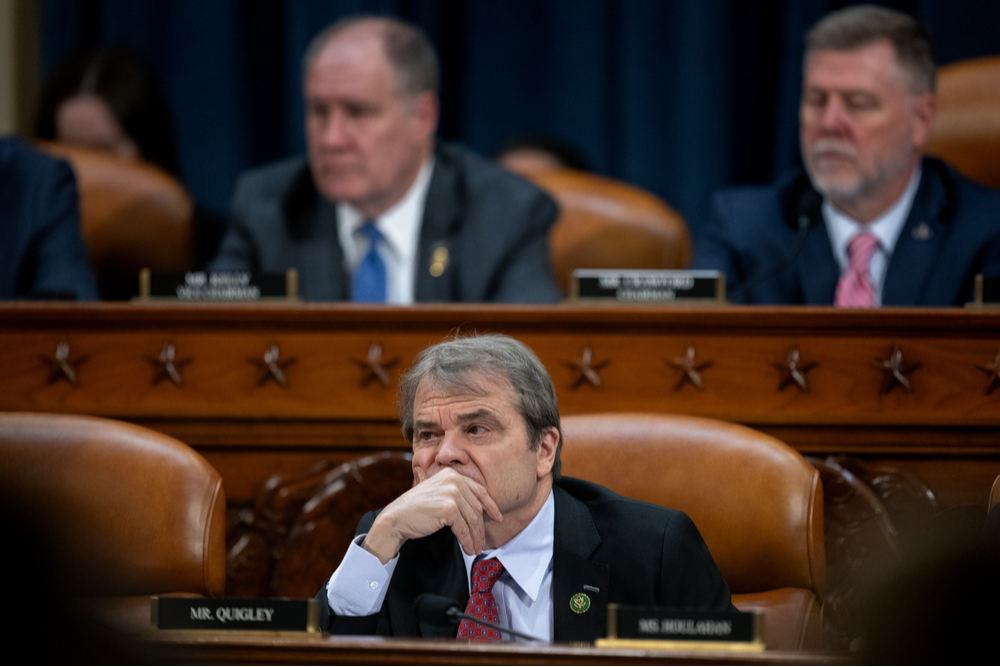 Congressman Quigley sits at a dais with his hand over his mouth