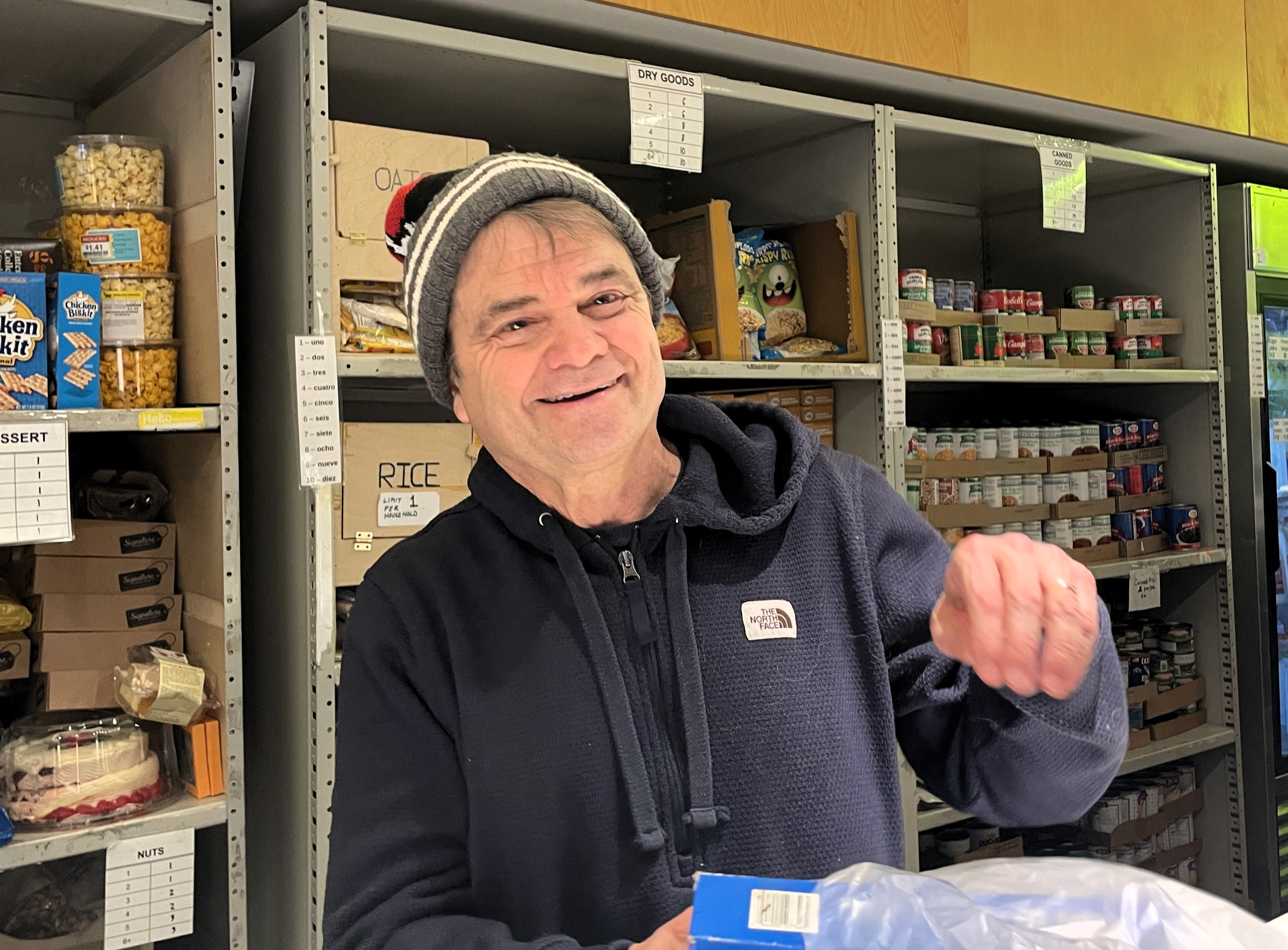 Quigley is at a counter bagging groceries with a smile on his face. He wears a Blackhawks beanie and ratty blue sweater.